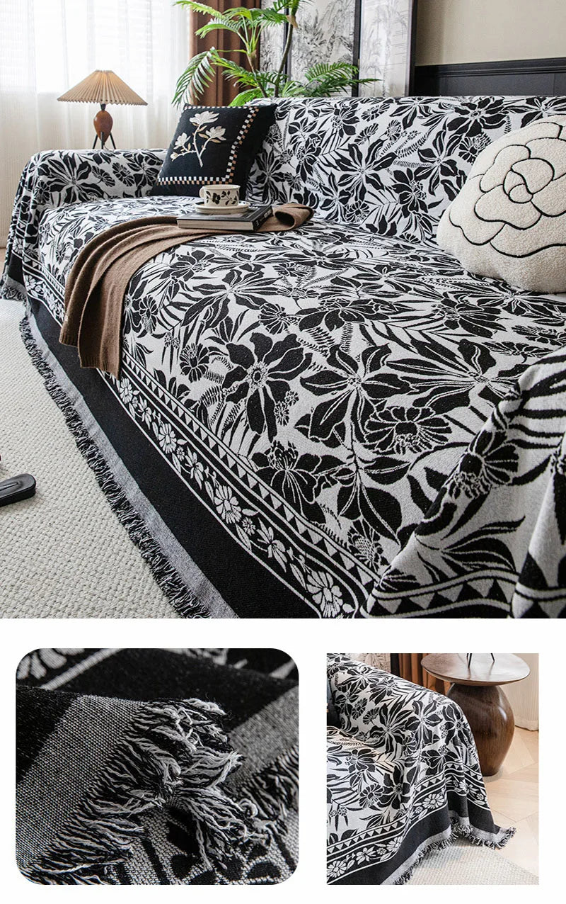 A black and white floral jacquard sofa blanket with tassels draped over a sofa.