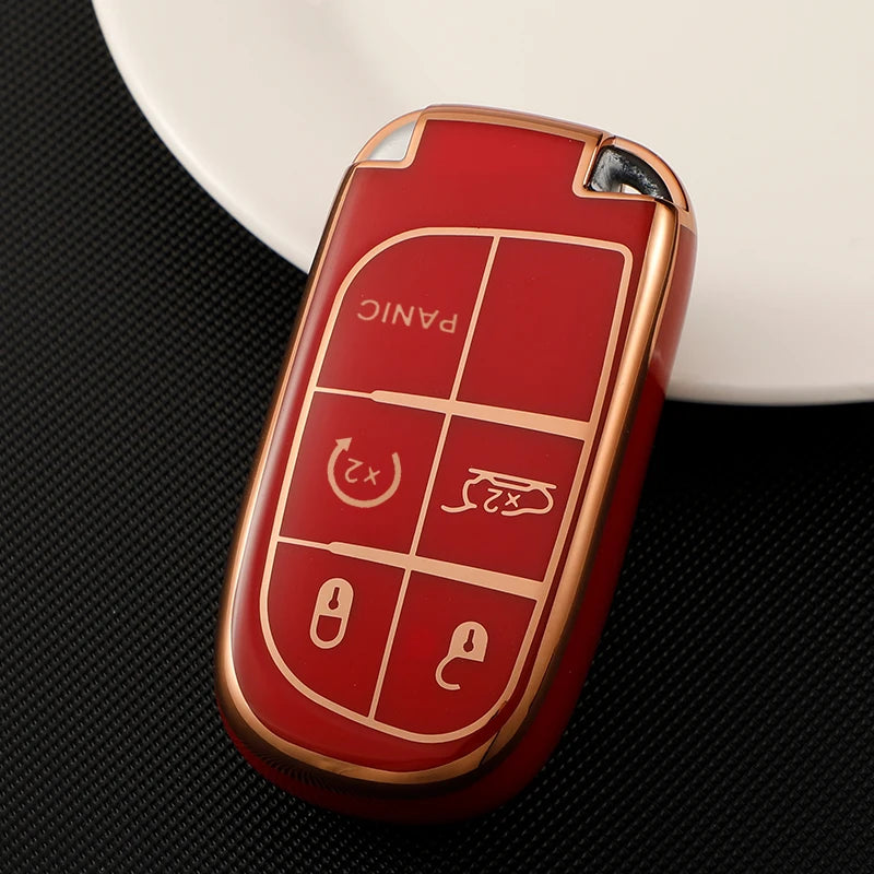 A red and gold durable TPU car key case cover resting on a black surface next to a white dish.