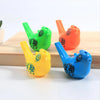 Three plastic bird whistles in green, orange, and blue are displayed on a wooden surface.