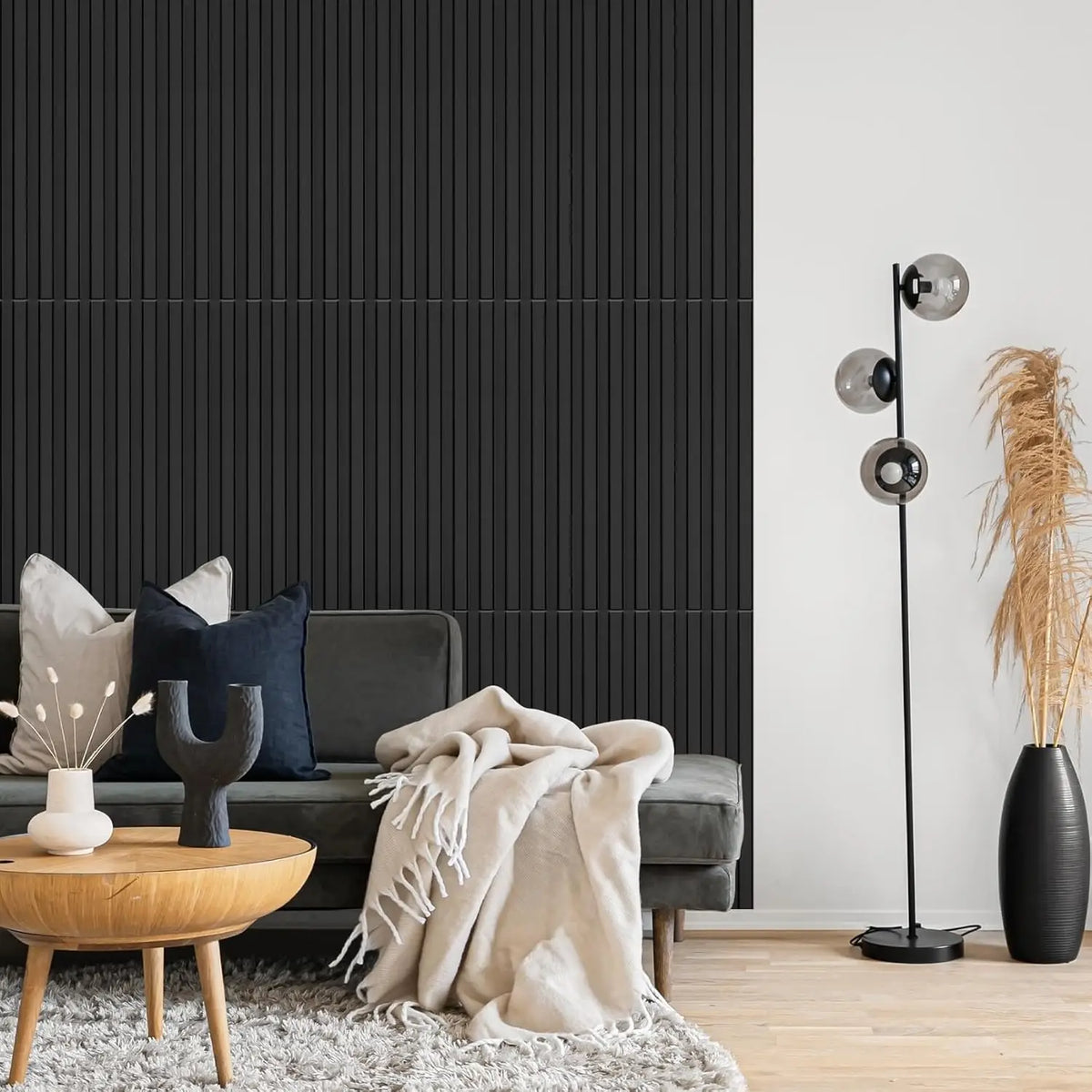 A modern living room featuring a dark slat wall panel, a gray sofa, and a floor lamp with dried grasses.