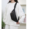 Un sac banane en nylon noir avec une sangle dorée porté par une personne en sweat blanc.