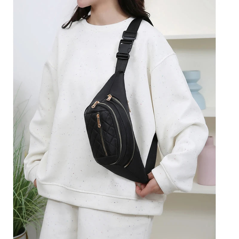 Un sac banane en nylon noir avec une sangle dorée porté par une personne en sweat blanc.