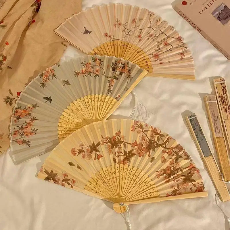 A collection of light wood and bamboo folding fans with delicate floral designs arranged on a white surface.