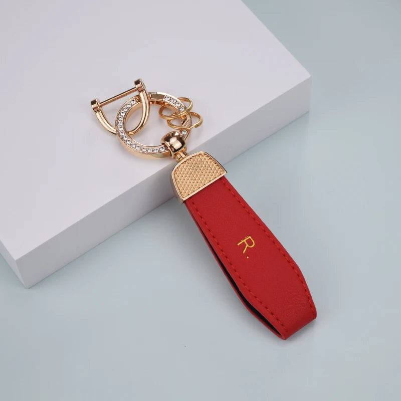 A red leather key fob cover with a gold-toned chain and ring attached, resting on a white surface.