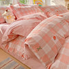 Pink plaid duvet cover set with matching pillow shams and a small stuffed animal on a bed.