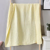 A yellow, textured muslin cotton blanket hanging on a wooden rack.
