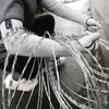 A person wearing gray cut-resistant arm sleeves is handling a large bundle of silver wire.
