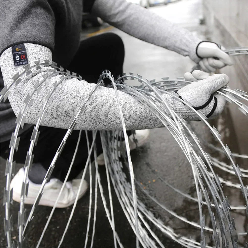 A person wearing gray cut-resistant arm sleeves is handling a large bundle of silver wire.