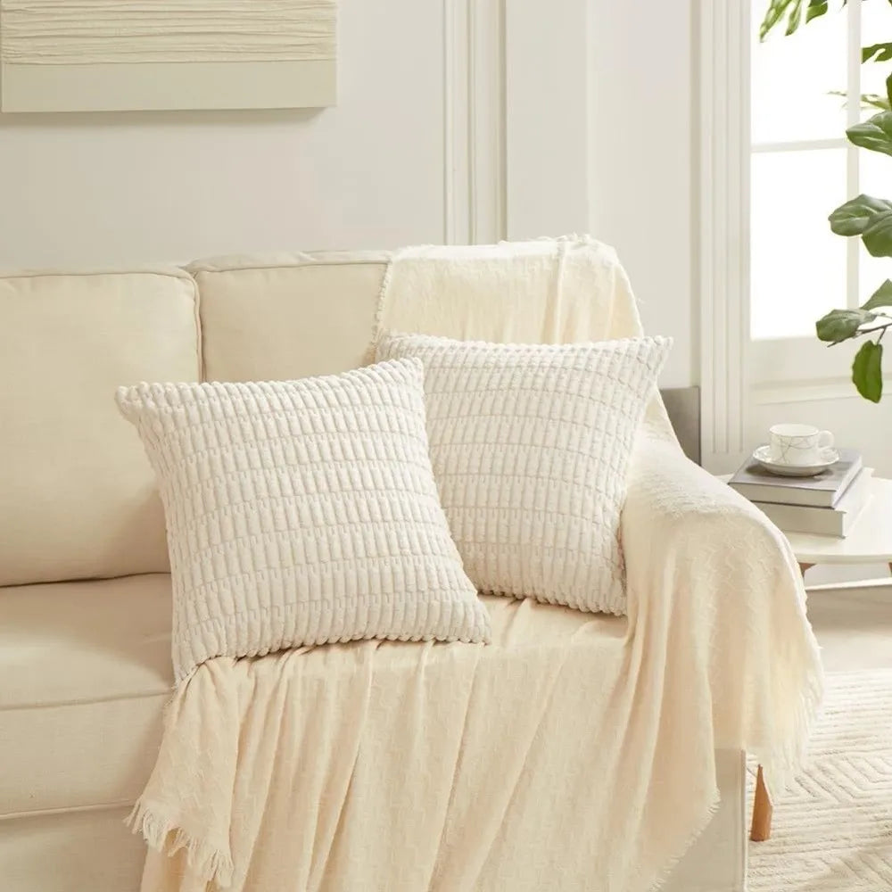 A close-up of a cream and white reversible corduroy pillowcase with a striped velvet design resting on a light-colored sofa.