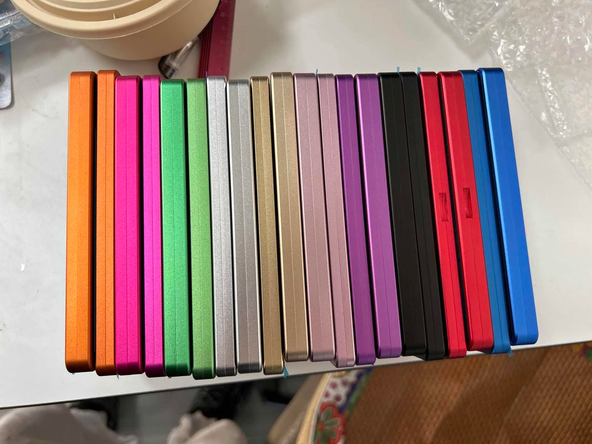 A row of colorful trading card protective display cases with various colored spines arranged horizontally.