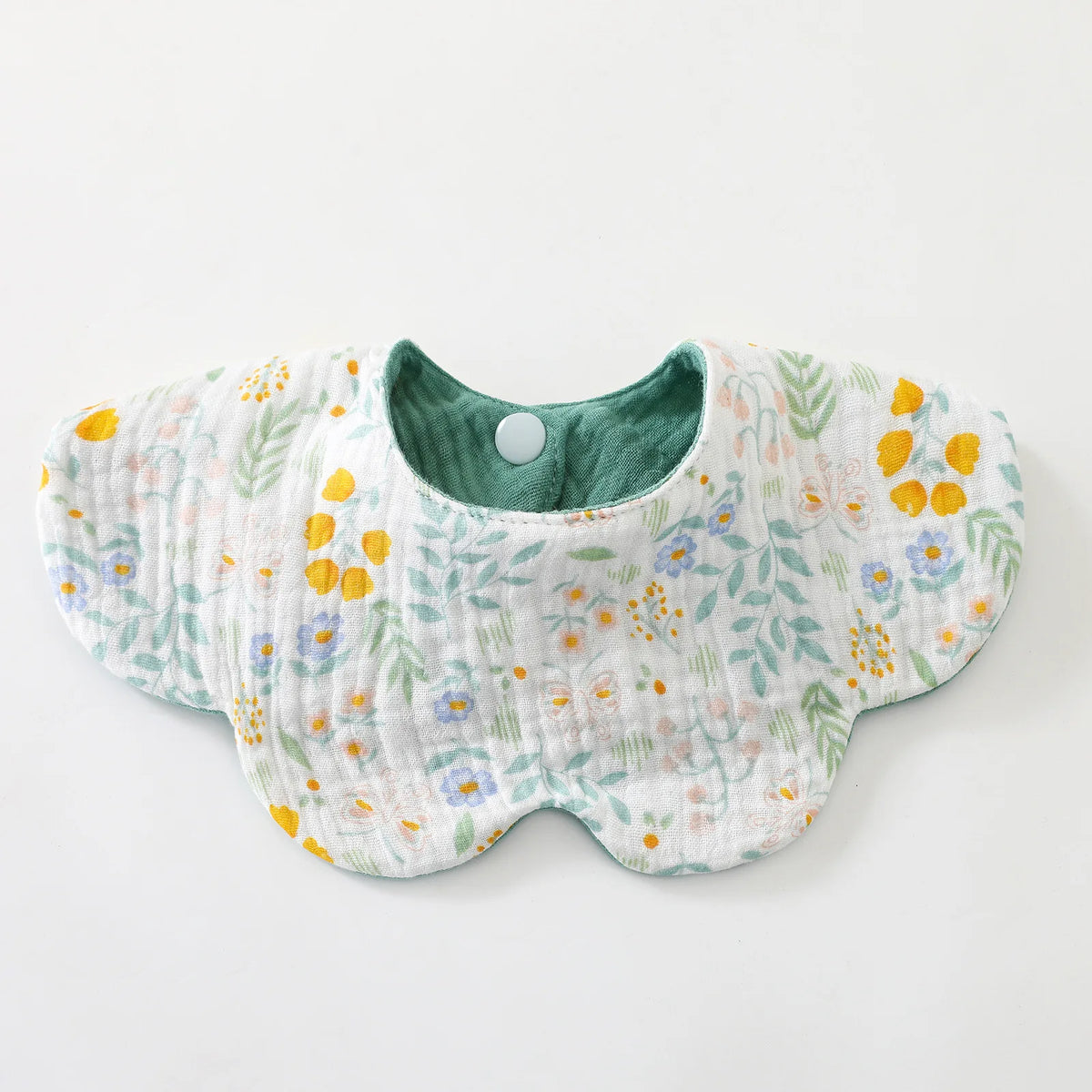 A white cotton baby feeding bib with a green interior and a floral pattern of yellow and blue flowers.