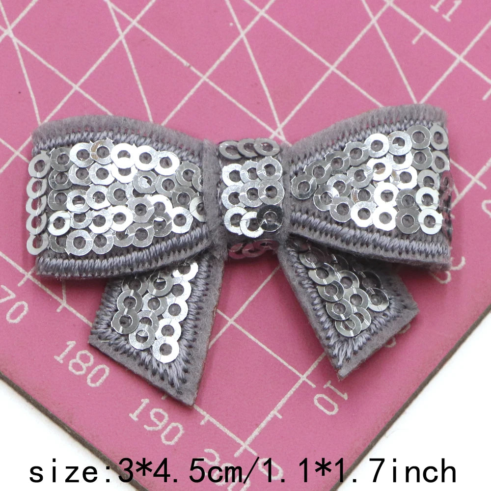 A silver sequin bow patch for DIY crafts shown on a pink ruler.