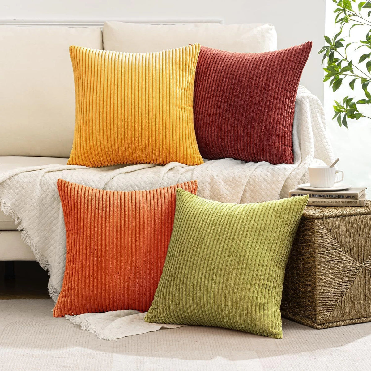 A collection of four vertical ribbed corduroy throw pillows in shades of orange, terracotta, and olive green on a white sofa.