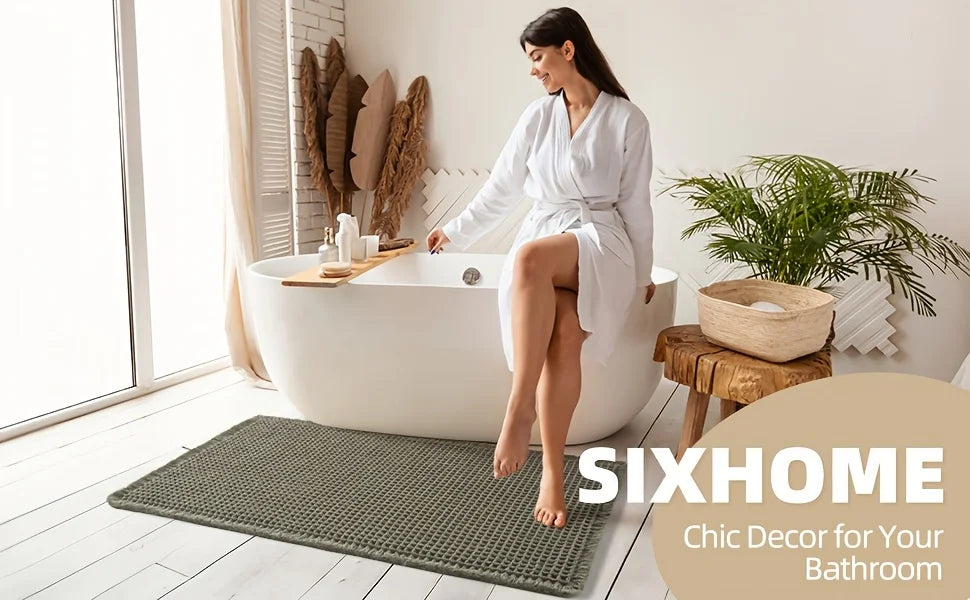 A woman sits in a white bathtub surrounded by natural decor, with a green waffle weave bath mat on the floor.