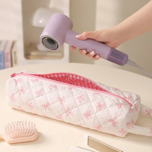 Una mano usa un organizador plegable para el pelo morado con detalle de lazo, junto a un estuche acolchado rosa y un alfiler.