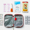 A compact travel medicine organizer bag is shown open, displaying various medical supplies and a blister pack of medication.