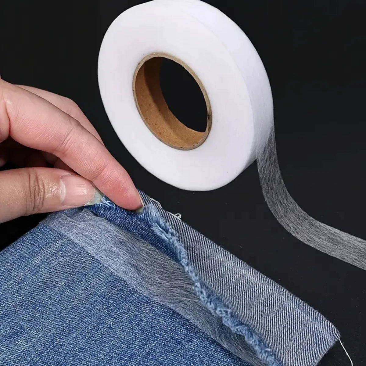 A hand is applying no-sew iron-on hem tape to the edge of a denim garment.