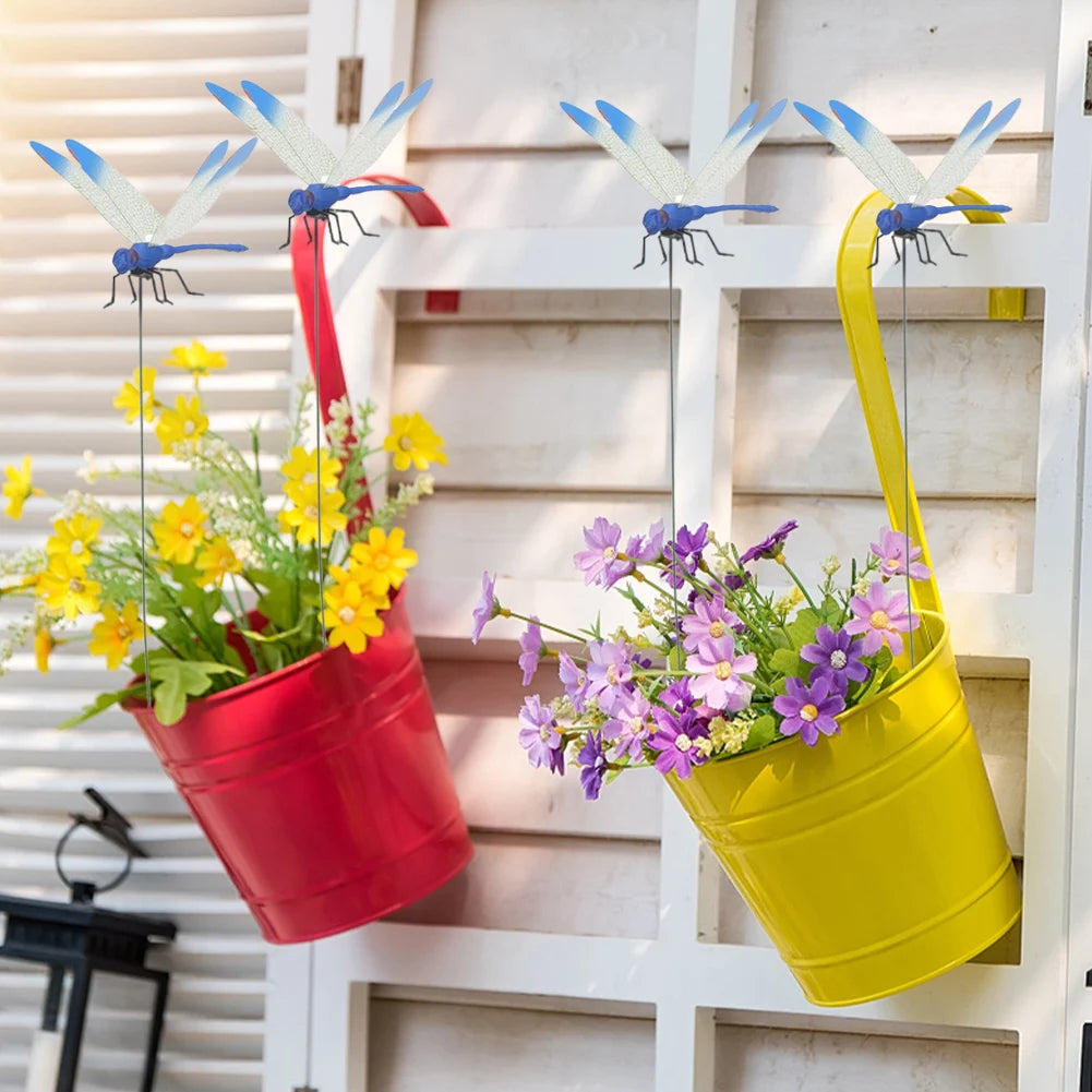 Yellow and red pots filled with flowers and dragonfly clips hanging on a white wooden fence.