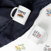 Eine weiße Tasse mit einem inspirierenden Zitat liegt auf einem dunkelgrauen Stoff.