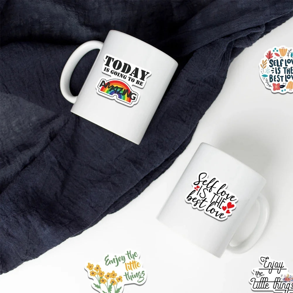 Eine weiße Tasse mit einem inspirierenden Zitat liegt auf einem dunkelgrauen Stoff.
