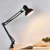 A black adjustable swing arm desk lamp is positioned over a wooden desk with open books.
