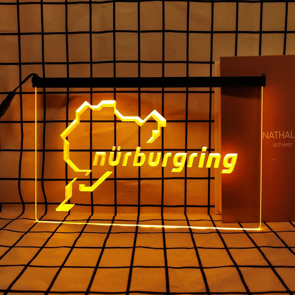 A neon sign shaped like a stylized mountain silhouette with the word Nürnbergring glowing bright yellow on a dark grid backgr