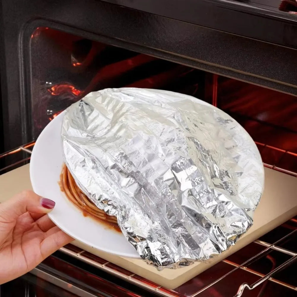 A hand holds a piece of food wrapped in aluminum foil inside an oven or grill.