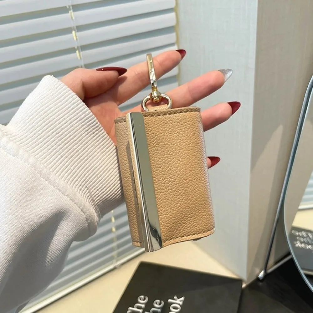 A hand holds a beige leather retractable keychain tote bag with a silver clasp against a light background.