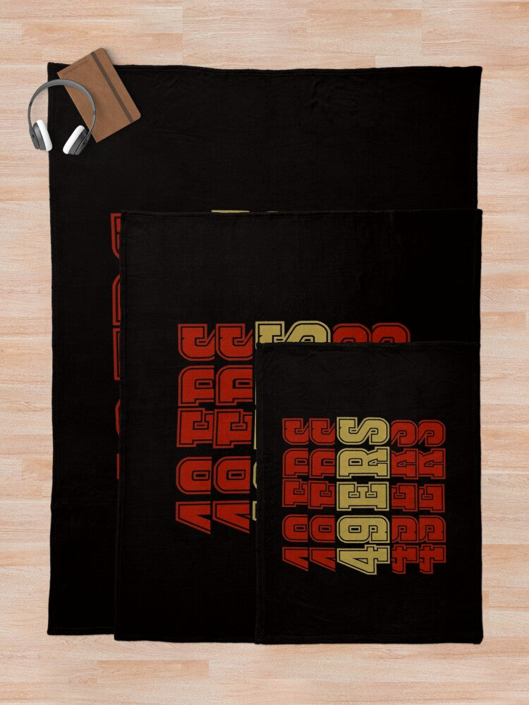 A black knit throw blanket featuring the 49ers team logo in red and gold colors.