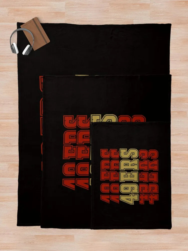 A black knit throw blanket featuring a repeating pattern of red and yellow letters.