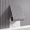 A roll of striped wood-look peel-and-stick wall panels is being installed on a vertical gray slat wall.