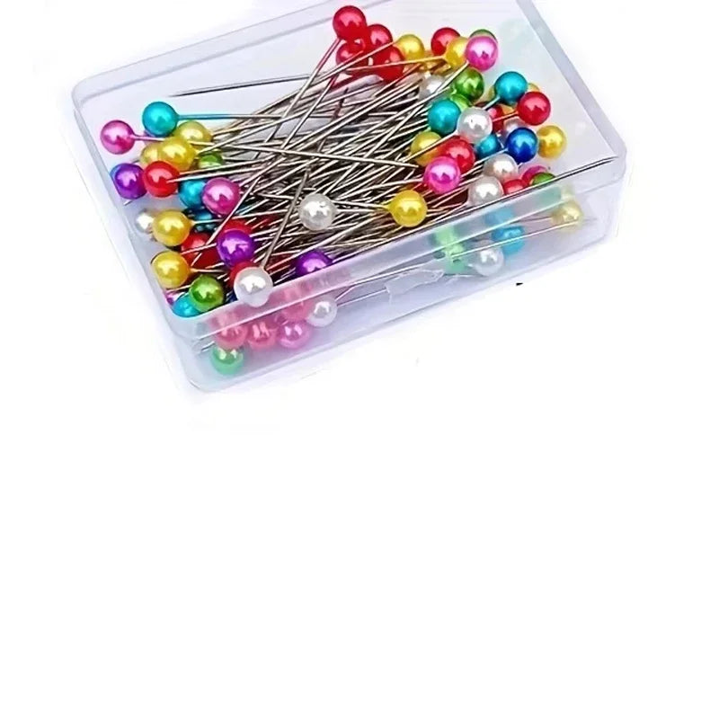A clear container filled with various colored pearlized ball head sewing pins for fabric crafting.