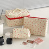 A quilted white makeup bag with a red trim and heart pattern is shown next to various makeup products.