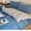A light blue quilted duvet cover set with matching pillowcases and a white throw blanket on a bed.