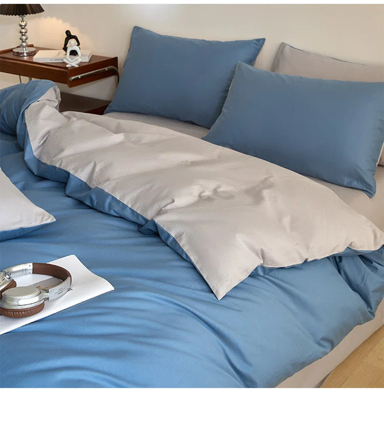 A light blue quilted duvet cover set with matching pillowcases and a white throw blanket on a bed.
