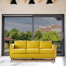 A bright yellow sofa placed in front of a large window with greenery and buildings visible outside.