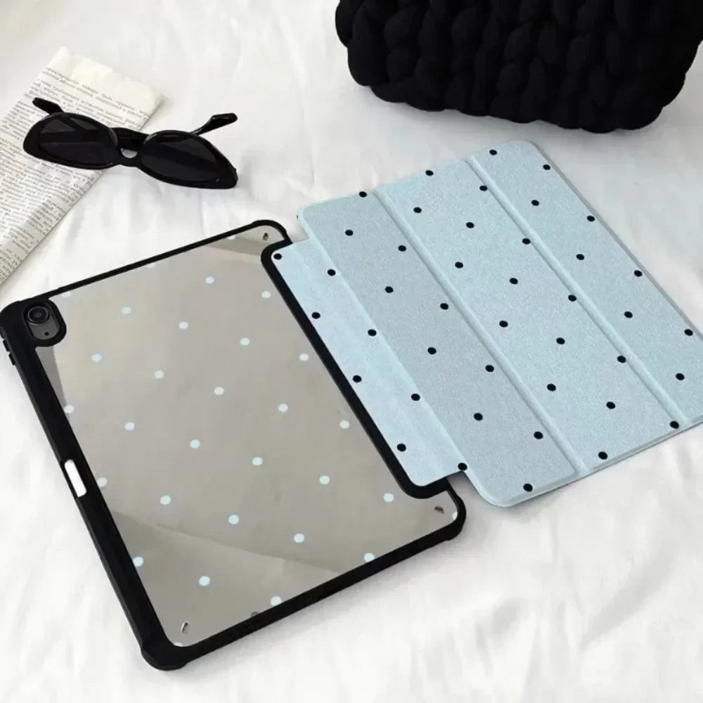 Silberes iPad mit Schutzhülle mit dekorativen Bleistiftfächern, neben Sonnenbrille und schwarzem Stoff