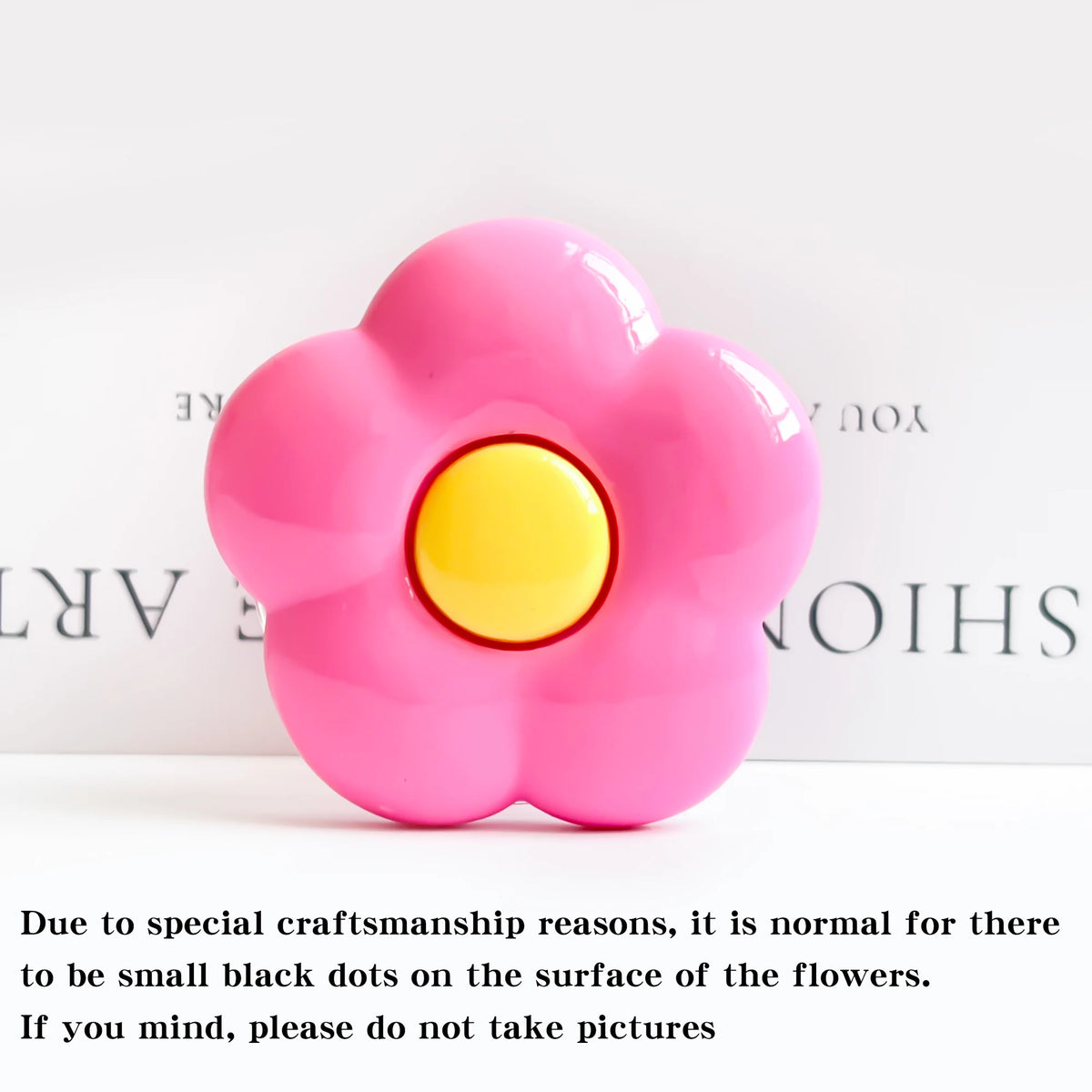 A pink flower shaped foldable phone grip stand with small black dots on the surface.