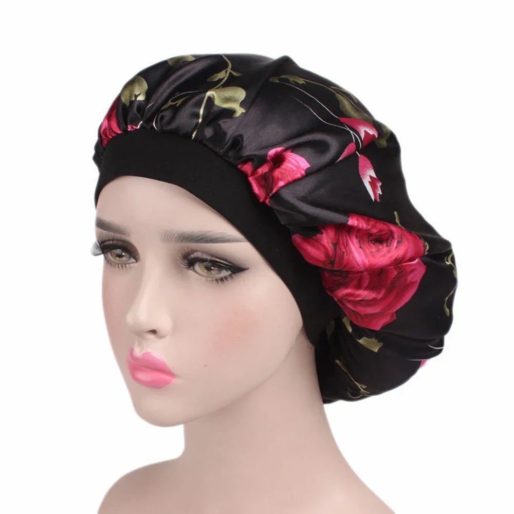 A black satin hair bonnet with a floral print featuring pink and red roses, displayed on a mannequin head.