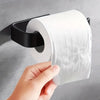 A hand is pulling a roll of white toilet paper from a black self-adhesive holder mounted on a gray wall.