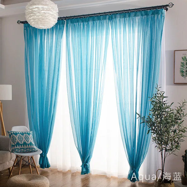 Light blue sheer voile curtains with rod pockets filtering soft light through a window.