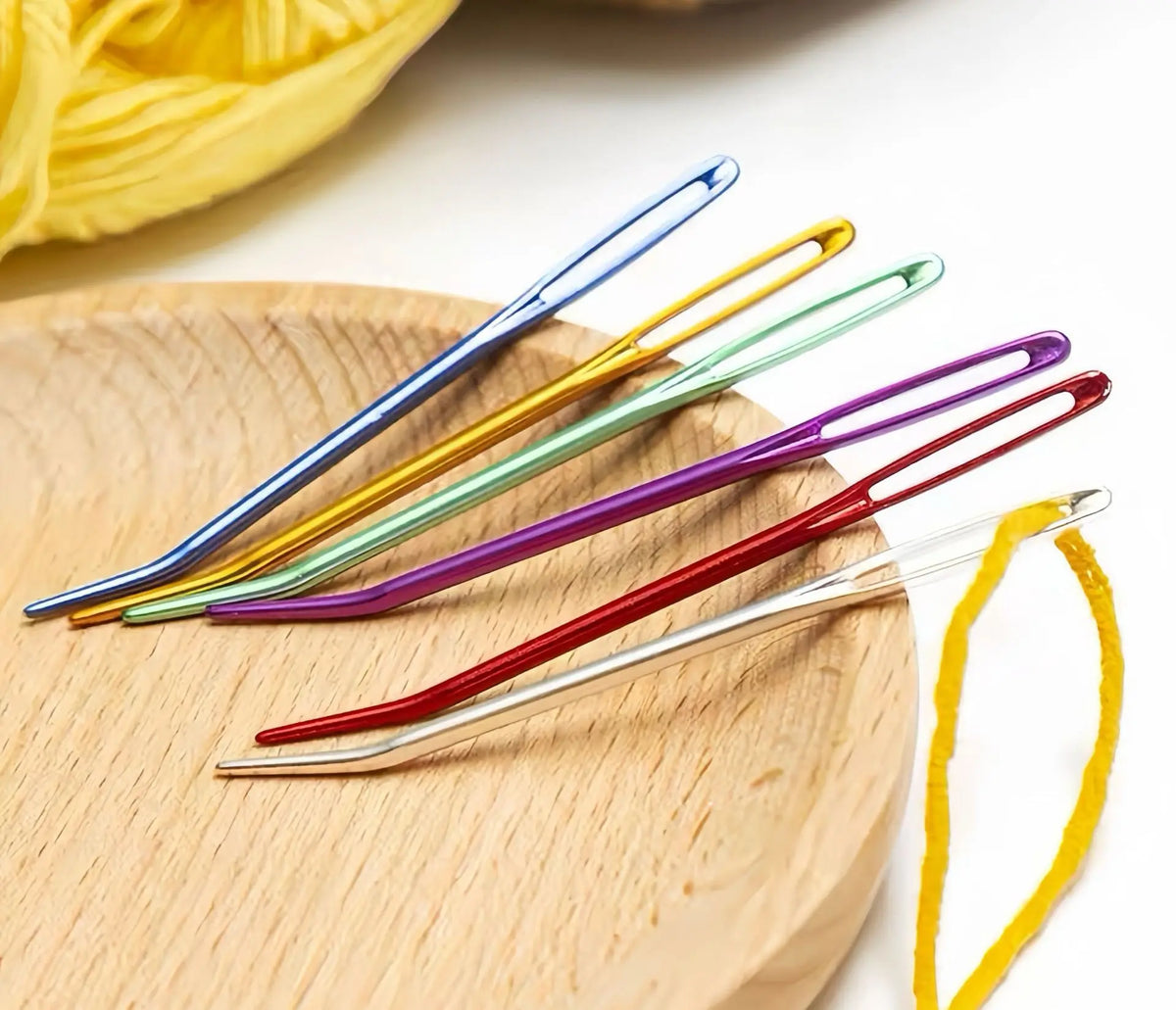 A collection of twenty large eye tapestry needles in various colors, including blue, yellow, green, and purple, resting on a 