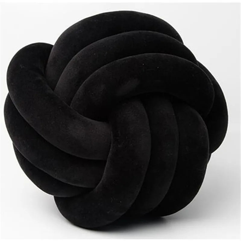 A round, black velvet throw pillow with a tightly knotted texture.