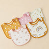 A collection of pastel colored cotton baby bibs in various shapes and patterns laid out on a light background.