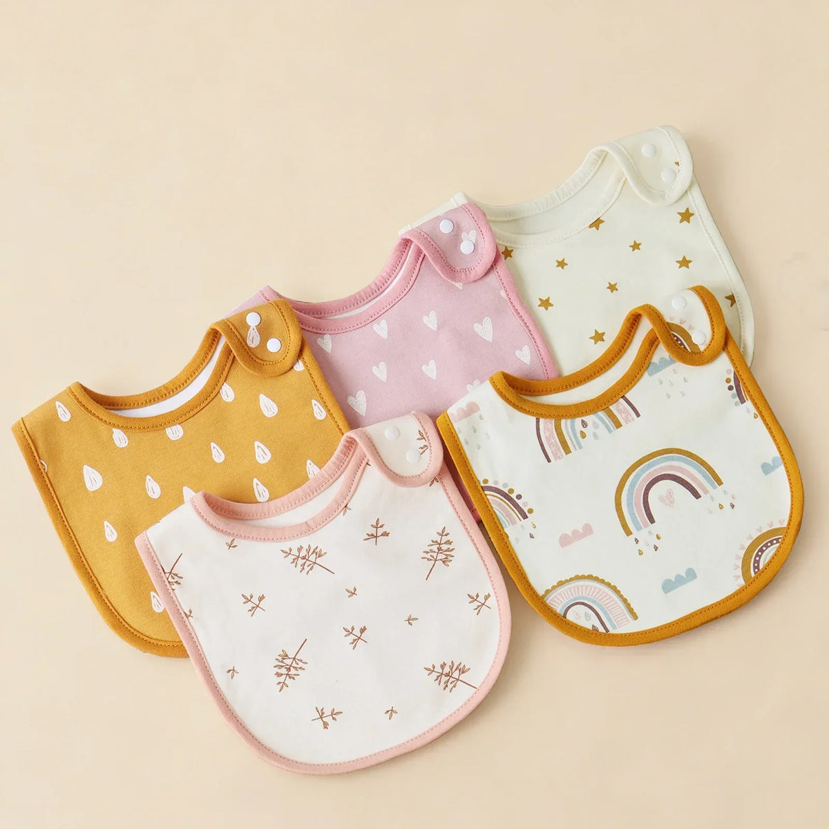 A collection of pastel colored cotton baby bibs in various shapes and patterns laid out on a light background.