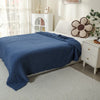 A navy blue soft muslin cotton blanket draped over a white bed with a cream and brown floral accent pillow.
