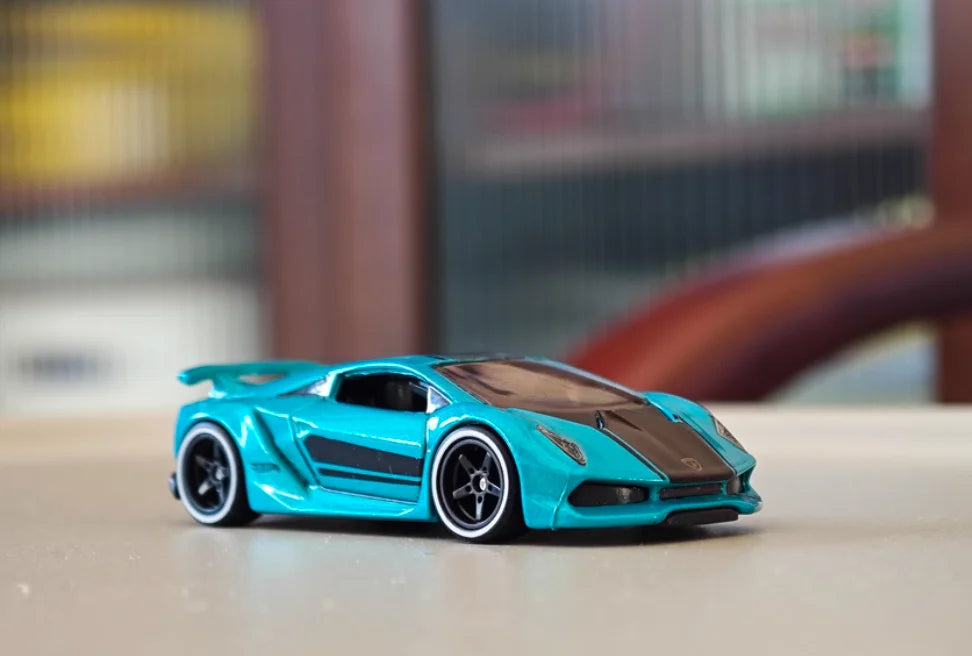 A bright turquoise 1:64 scale alloy sports car model with black accents, shown on a light surface.