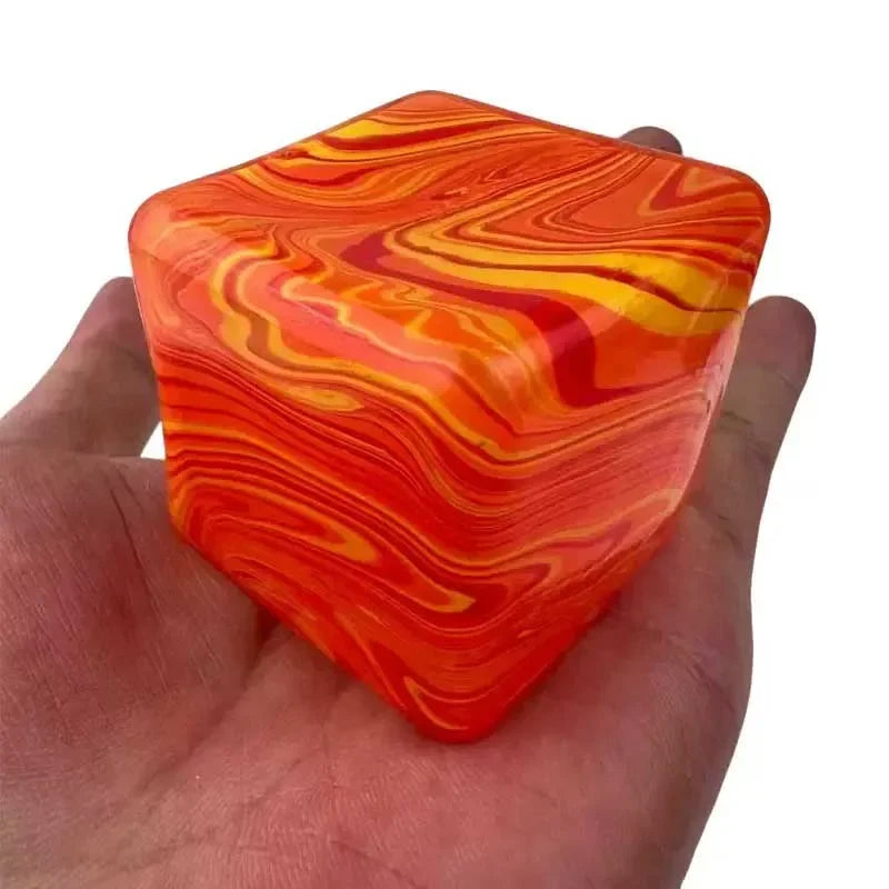 Une main tient un cube de jeu en gel anti-stress marbré orange et jaune.