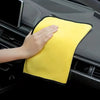 A hand is holding a bright yellow microfiber cleaning towel in the interior console of a car.