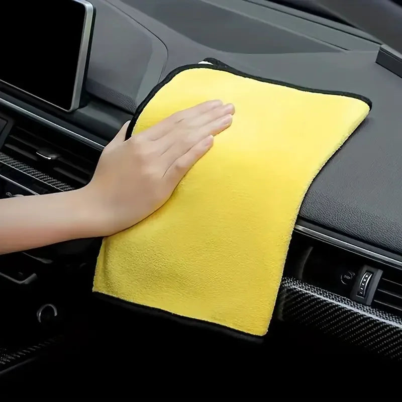 A hand is holding a bright yellow microfiber cleaning towel in the interior console of a car.
